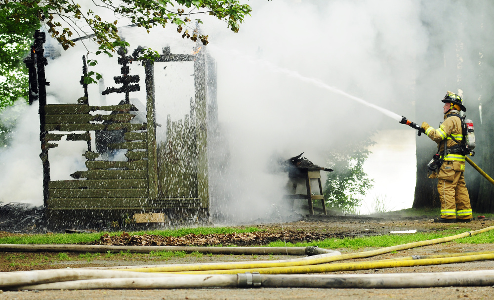An Augusta firefighter sprays a hot spot on Tuesday after the crew put out a fire in a shed on Albee Road in Augusta.