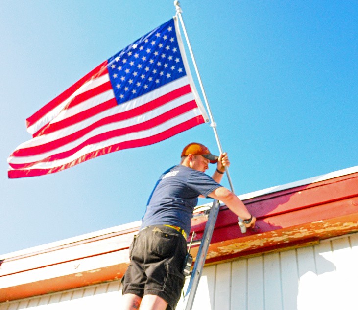 Nicholas Kimball straightens out the American flag last week at the fire house in Randolph. It's the same style as the ones that probably will go up in town Saturday now that a private donor has paid for additional liability insurance.