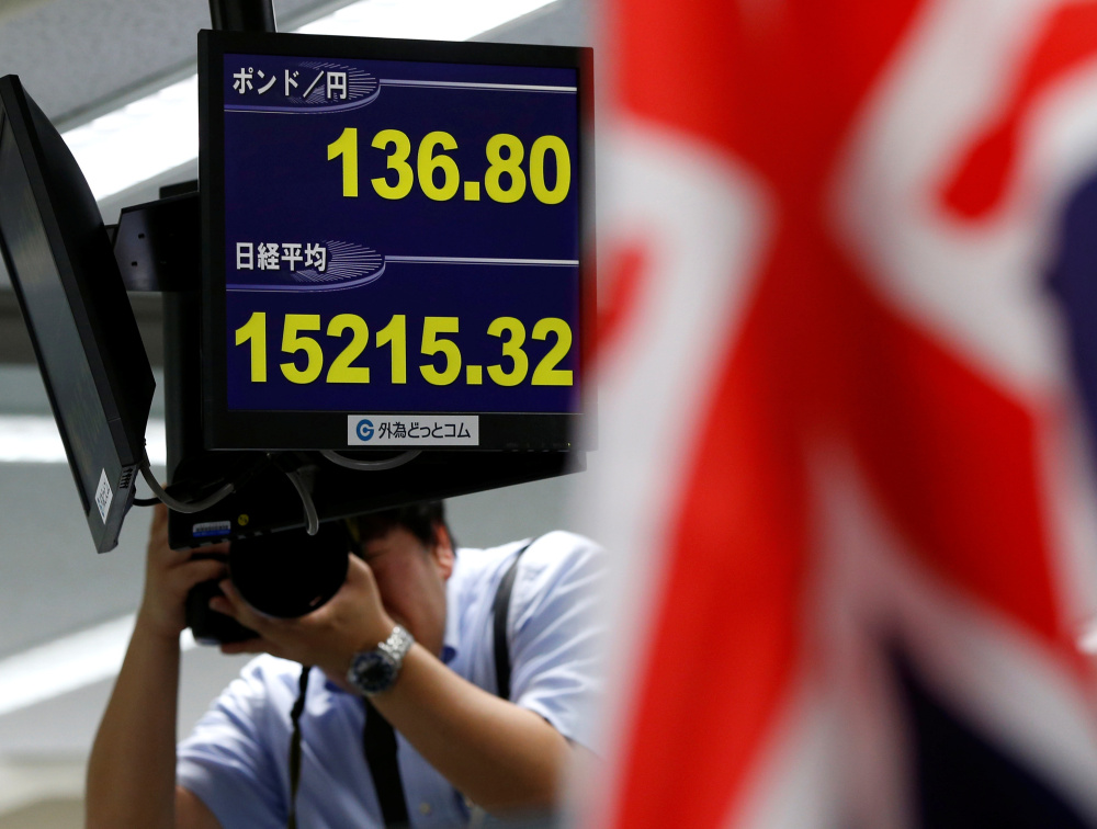 A photographer take photos of monitors displaying the yen's exchange rate against the British pound and Japan's Nikkei share average Monday at a trading company in Tokyo.