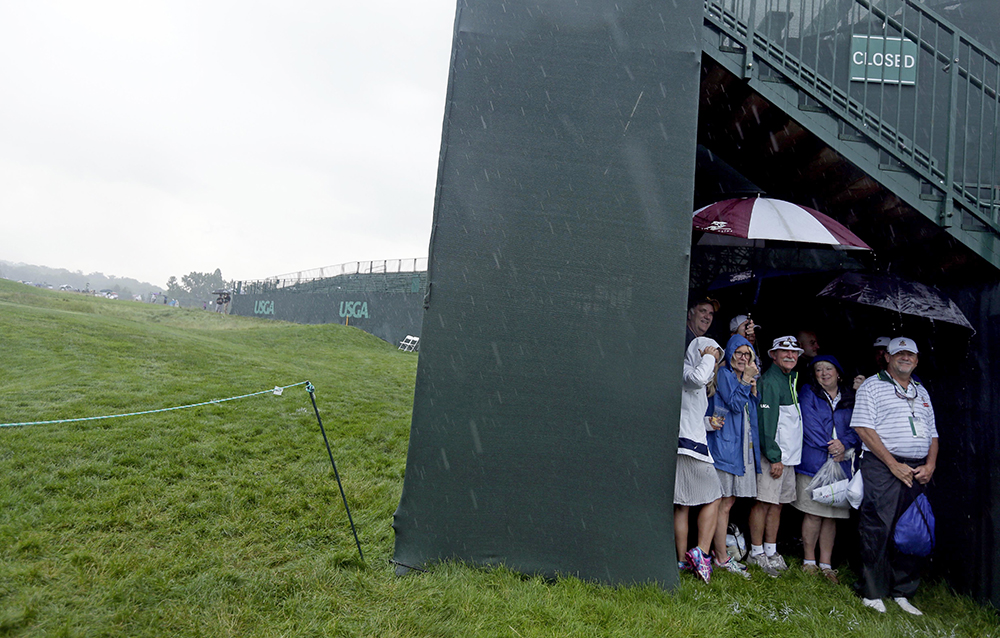 Fan hide from the rain during a delay in the first round of the U.S. Open golf championship at Oakmont Country Club on Thursday in Oakmont, Pa. Associated Press