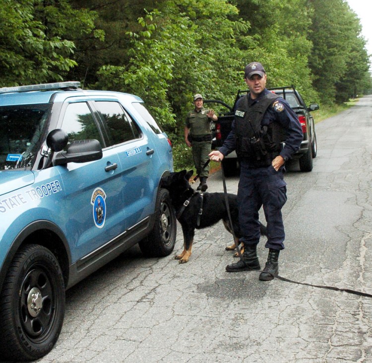 Maine State Trooper G.J. Neagle and his police dog, Draco, and Game Warden Steve Couture leave the woods on Bellsqueeze Road in Clinton after they found Michael Savage, who police said fled from a Hinckley Road home when police arrived in responding to an anonymous 911 call.