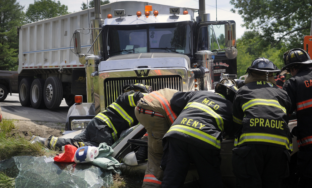Firefighters extricate two people trapped Tuesday in a vehicle that collided with a tractor-trailer on Route 126 in Litchfield. One person in the vehicle died while two others were transported to area hospitals. The driver of the truck was uninjured.