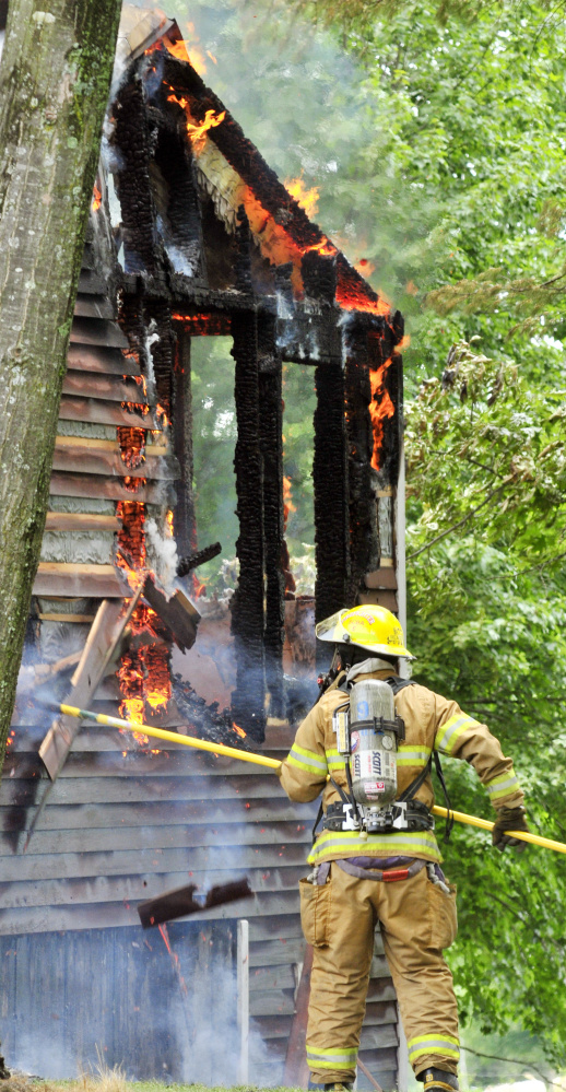A firefighter pulls off siding to expose flames Sunday at 35 Holway Road in Sidney.