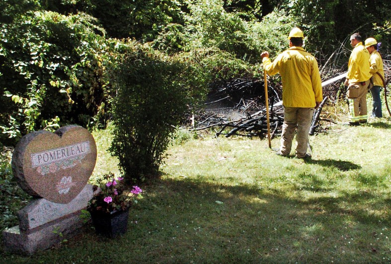 Waterville firefighters extinguish a fire in brush beside gravesites at the St. Francis Cemetery in Waterville on Thursday. Police said Friday they have a suspect in both that fire and an earlier one at adjacent Pine Grove Cemetery.
