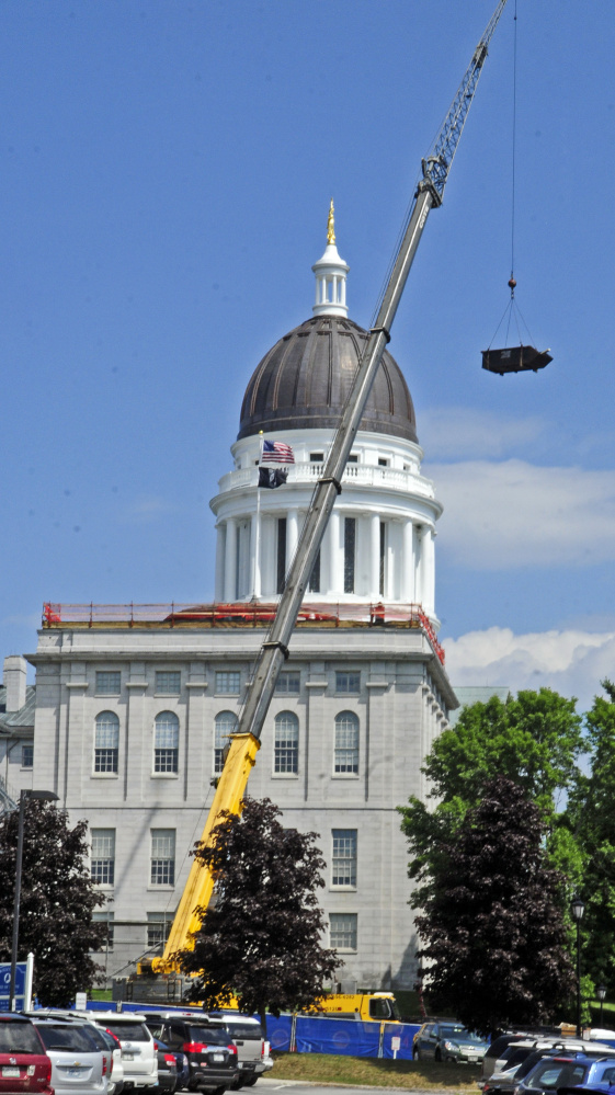 A crane lowers a dumpster off the roof of the Senate wing of the State House on Tuesday in Augusta, where workers are making repairs.