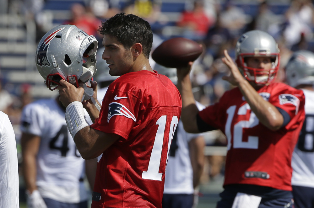 New England Patriots quarterback Jimmy Garoppolo, left, removes his helmet as quarterback Tom Brady, right, winds up for a pass during training camp Thursday in Foxborough, Massachusetts.
