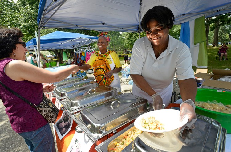 Mavis Kwakutse, right, of Scarborough, who is originally from Ghana, loads a plate of food for Leticia Foss of Sanford, who is originally from Mexico, during the Festival of Nations at Deering Oaks in Portland on Saturday. In the background collecting money is Kadiatu Moriba of Portland, who grew up in Sierra Leone. Shawn Patrick Ouellette/Staff Photographer