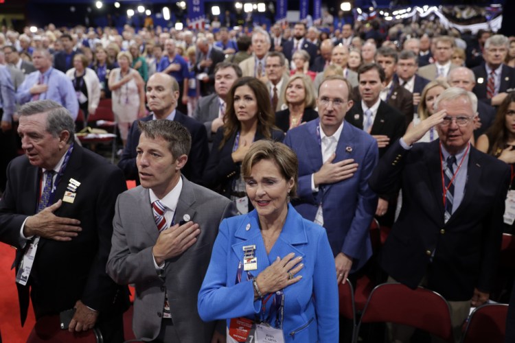 Alabama delegate Judy Carns, center in blue, and other delegates put their hands on their chests as they sing the national anthem during first day of the Republican National Convention in Cleveland, Monday, July 18, 2016.