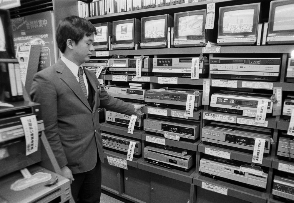 In this Dec. 15, 1981, file photo, a sales clerk at an electronics store in the Akihabara District of Tokyo, displays a stack of video cassette recorders which are on sale for 20 to 30 percent off. Japanese electronics maker Funai Electric Co. says it's yanking the plug on the world's last video cassette recorder. A company spokesman, who requested anonymity citing company practice, confirmed Monday that production will end sometime during the month, although he would not give a date.
