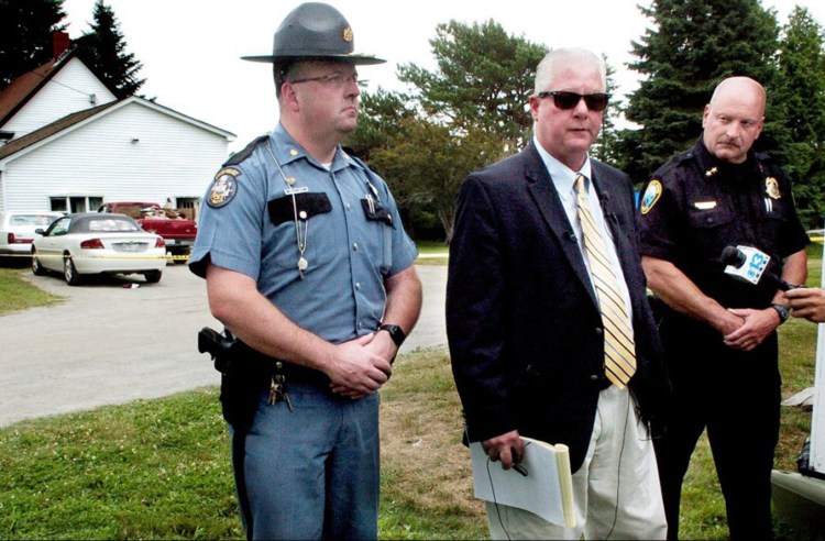 Maine State Police Lt. Brian McDonough, center, speaks about a possible home invasion Thursday that resulted in the death of one man and serious injuries to two others at the home in background off Main Street in Rangeley. At left is Maj. Brian Scott and at right is Rangeley Police Chief Russell French.