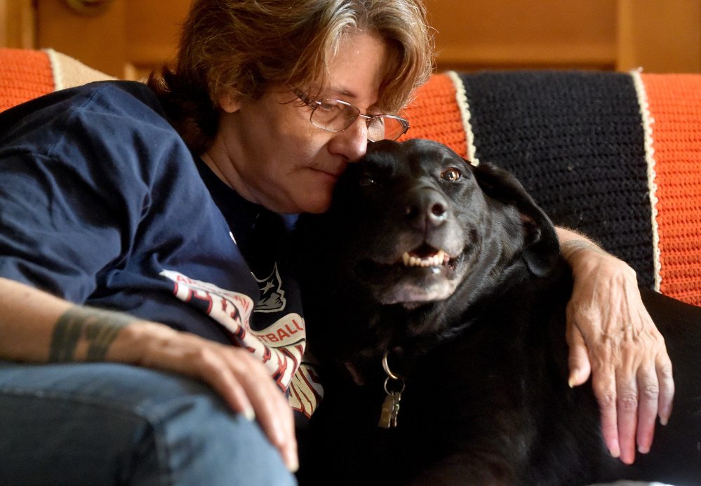 Eva St. Jean is comforted by her dog, Jasmine, as she talks about the struggle to find Waterville housing that will allow her to live with the 80-pound black Lab mix.