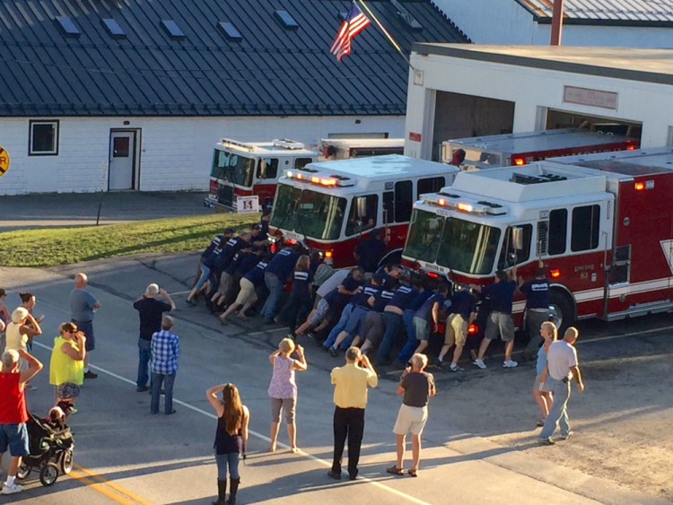 Monmouth firefighters push the department's two new engines into the station Thursday as part of a ceremony to officially place the vehicles into service. More than 30 fire department members helped with the push-in.