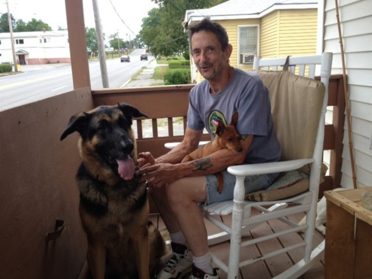 Gary Prentiss, 61, sits on the porch of his new home on Kennedy Memorial Drive in Waterville with his German shepherd, Mack, and miniature pinscher, Ginger. After having a tough time finding a place that would take his several animals, Prentiss was able to rent the house next door to his former house, which is in the background.