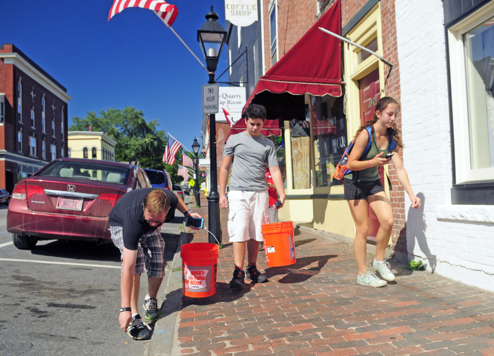 From left, Phillip Jones, Luke Robinson and Clarrissa Lettre pick up cigarette butts and other trash Saturday as they play Pokémon GO on Water Street in Hallowell.