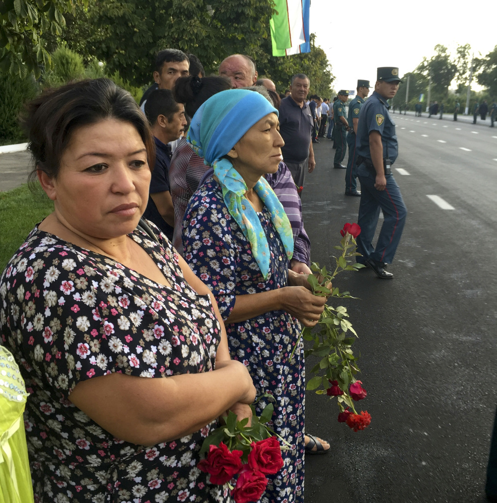 People hold flowers as they gather along the road under the Uzbekistan national flag to watch the funeral procession of President Islam Karimov in Tashkent, Uzbekistan, early Saturday. Karimov died of a stroke at age 78, the Uzbek government announced Friday.
Associated Press/ Umida Akhmedova