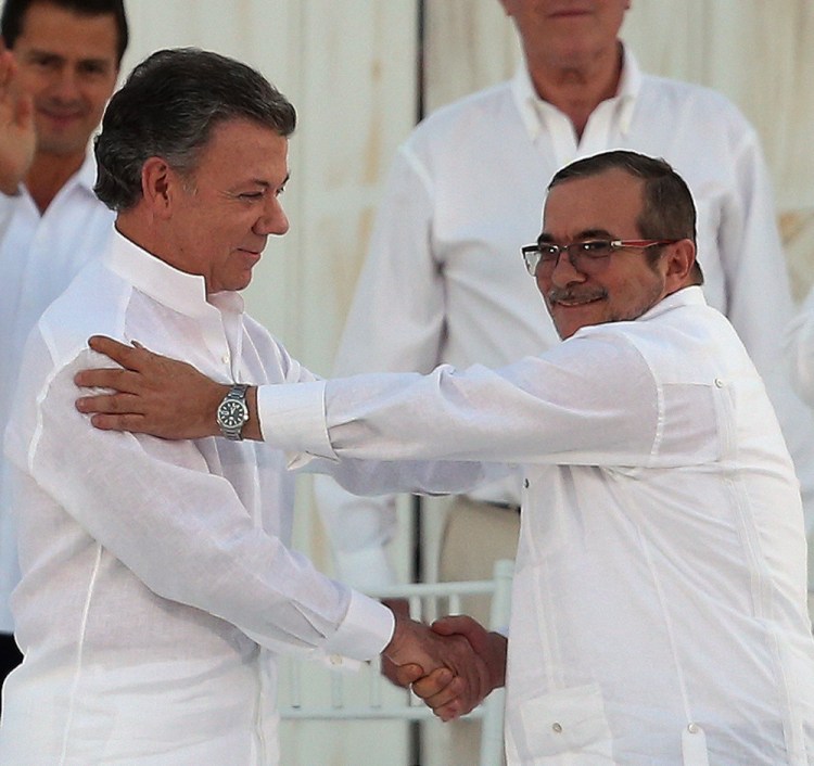 Colombia President Juan Manuel Santos, left, and the top commander of a longtime rebel army, Rodrigo Londono, shake hands after signing a peace accord Monday.