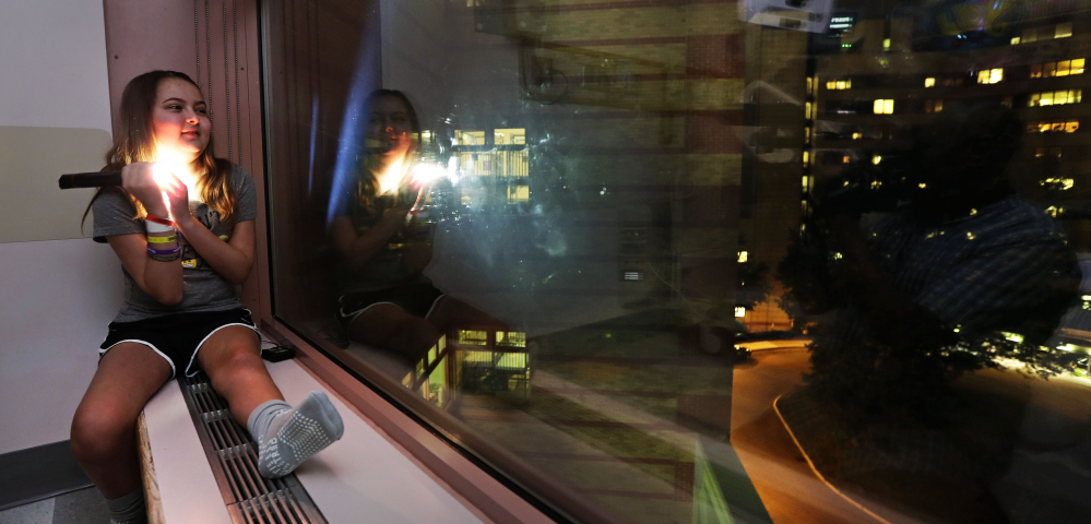 Olivia Stephenson of Lincoln, R.I., covers the lens of a flashlight as she messages back two light pulses, meaning "thank you," to people in surrounding buildings from her hospital room in Providence, R.I. Businesses around the Hasbro Children's Hospital flash their lights on and off every night as a way to say goodnight to sick children inside. At right, skyline lights illuminate downtown as seen from the hospital.