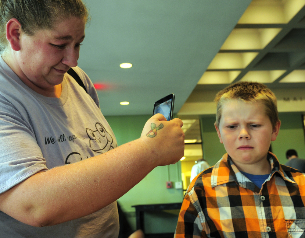 Blaze Moody, 7, of Guilford, right, makes a disapproving face after tasting a roasted cricket while his mother, Amber Moody, records it on her phone at the Entosense Inc. booth during Bug Maine-ia on Tuesday at the Maine State Museum in Augusta.