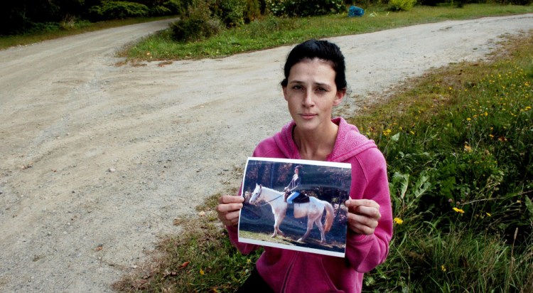Sierra Miner holds a photograph of her and her 4-year-old mare, Lucy, on Thursday at the spot she said someone drove onto her property in Canaan a day earlier and struck and dragged the tethered horse to her death. Miner became emotional and said, " I will now have to drive past the spot every day where my horse was murdered."