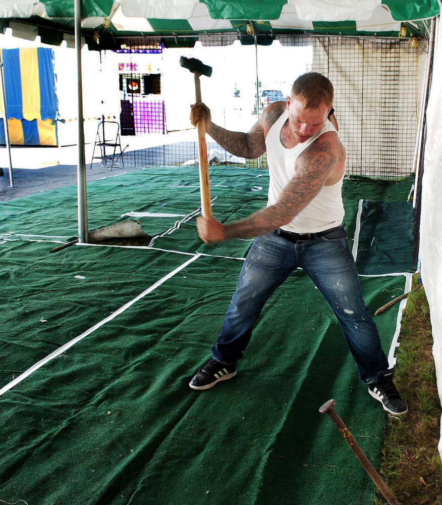 Tyler Stephenson swings a maul to pound in a stake to secure the tent for a leather goods booth Thursday at the Farmington Fair, which starts Sunday.