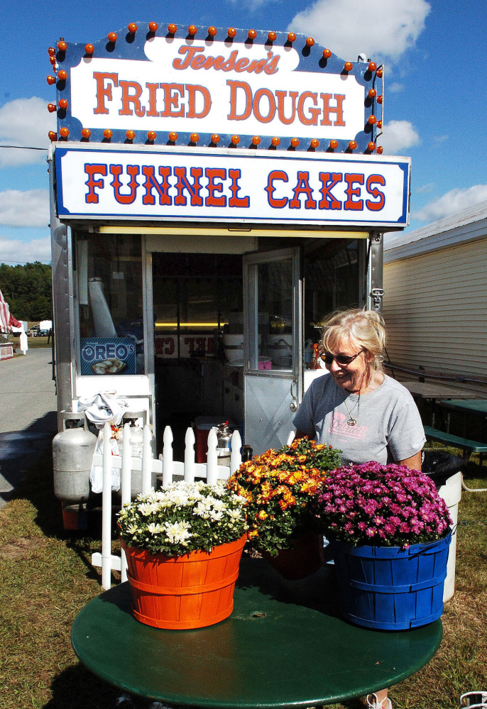 Linda Jenson arranges a flower display outside of her fried dough stand on Thursday for the Farmington fair, which begins Sunday.