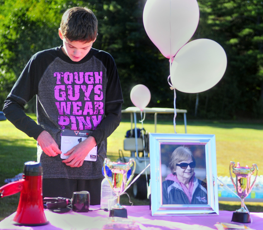 Standing behind a picture of his late grandmother, Lois Lajoie, race organizer Casey Gallant pins bib number 1 onto his shirt before at the Miles Across Maine for Breast Cancer Awareness on Saturday at University of Maine of Augusta.
