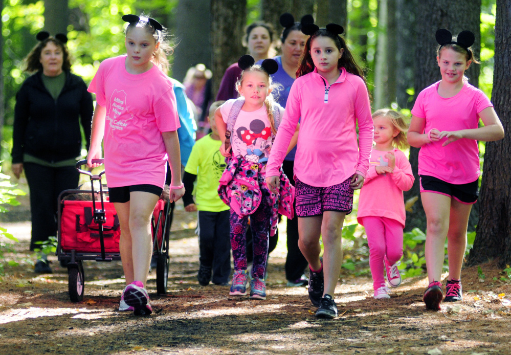 Participants, many wearing pink and mouse ears, walk through the woods during the Miles Across Maine for Breast Cancer Awareness on Saturday at University of Maine of Augusta.