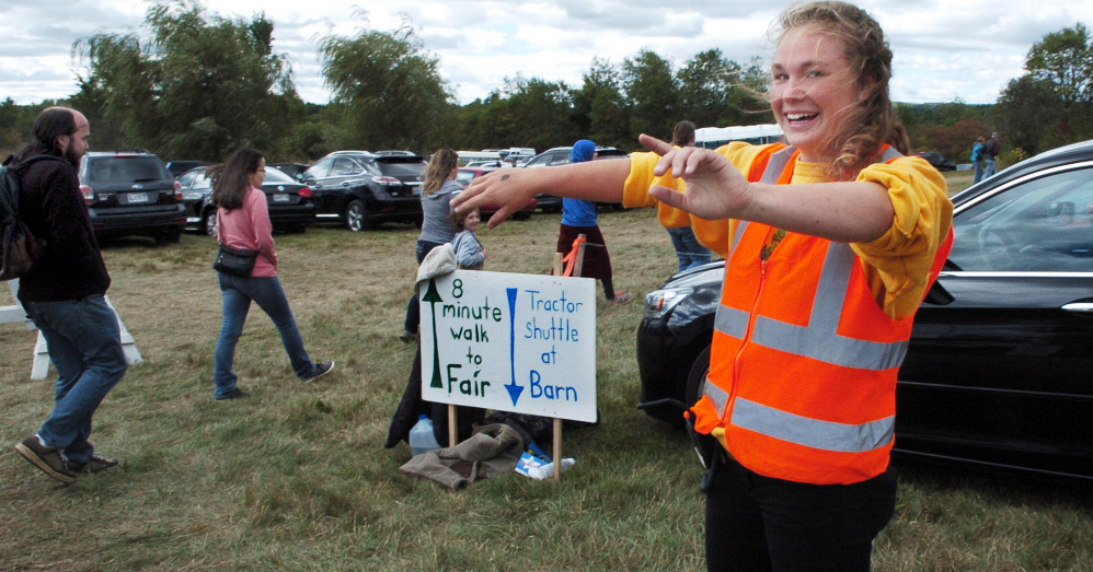 Volunteer Maureen Grubb stops motorists in a parking lot for pedestrians walking on a trail to the Common Ground Country Fair in Unity on Sunday. Grubb said she has been a volunteer at the fair for seven years. " I love doing this because everyone is so happy to be at this community fair," she said.