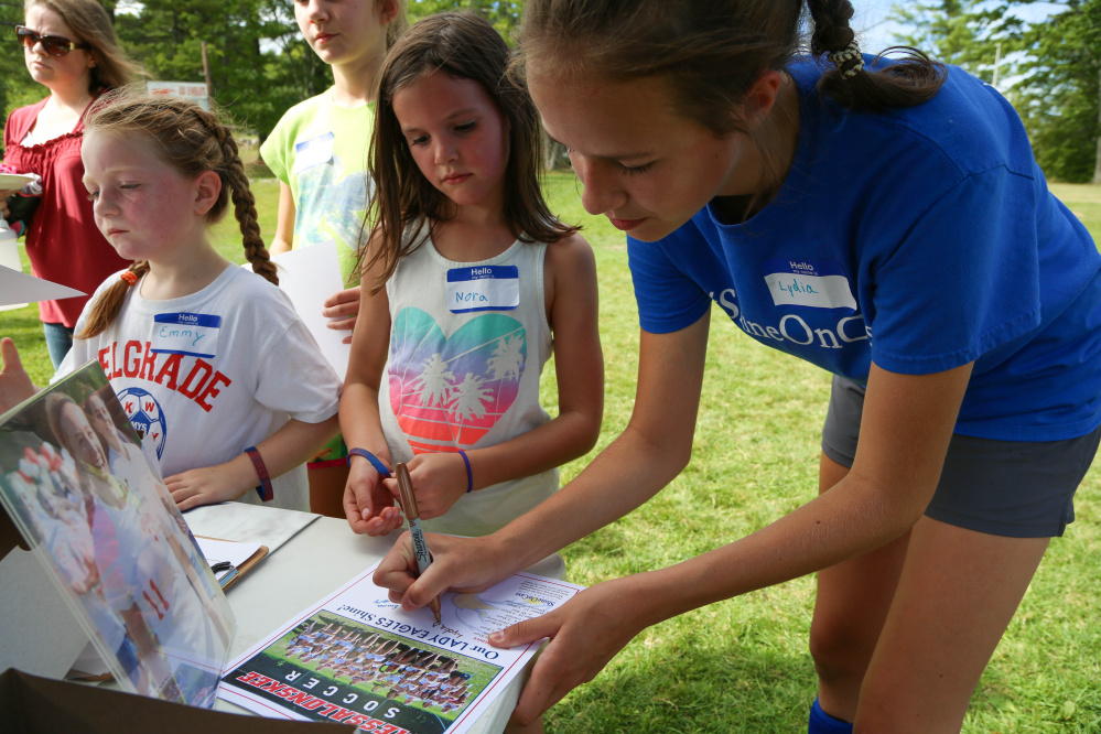 Messalonskee High School girls soccer player Lydia D'Amico, right, autographs a team poster for Nora Kalback, center, while Emmy Dunbar, left, waits her turn at Shine On Saturday Sept. 10 in Oakland.