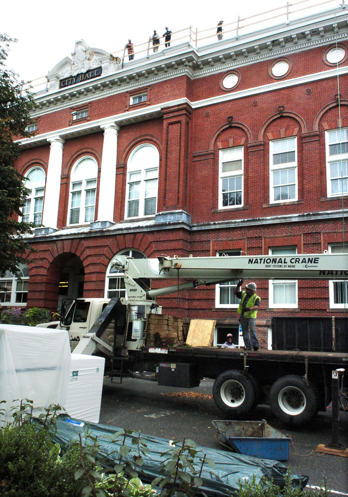 Workers on top of Waterville City Hall wait for others with Roofing Systems of Maine to use a crane to lift materials while replacing the building's roof Tuesday.