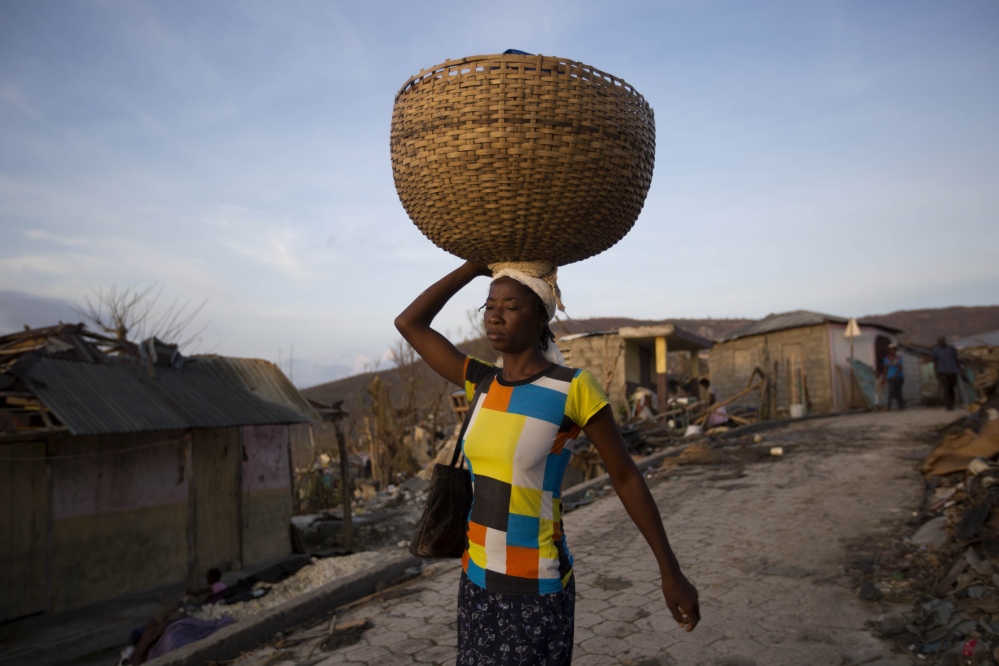 A woman walks as she sells bread near destroyed homes by Hurricane Matthew in Jeremie, Haiti on Monday, Oct. 10, 2016. Almost a week after Matthew's assault,  power is still out, water and food are scarce, and officials say that young men in villages along the road between the hard-hit cities of Les Cayes and Jeremie are putting up blockades of rocks and broken branches to halt convoys of vehicles bringing relief supplies. (AP Photo/Dieu Nalio Chery)