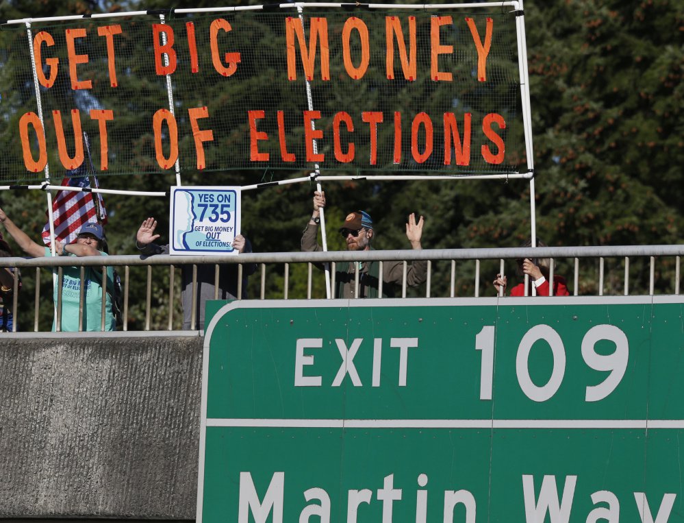 Supporters of an initiative in Lacey, Wash., hold a banner during the evening commute in Lacey, Wash., in September. Voters increasingly are upset with the way campaigns are paid for disproportionately by big-money donors