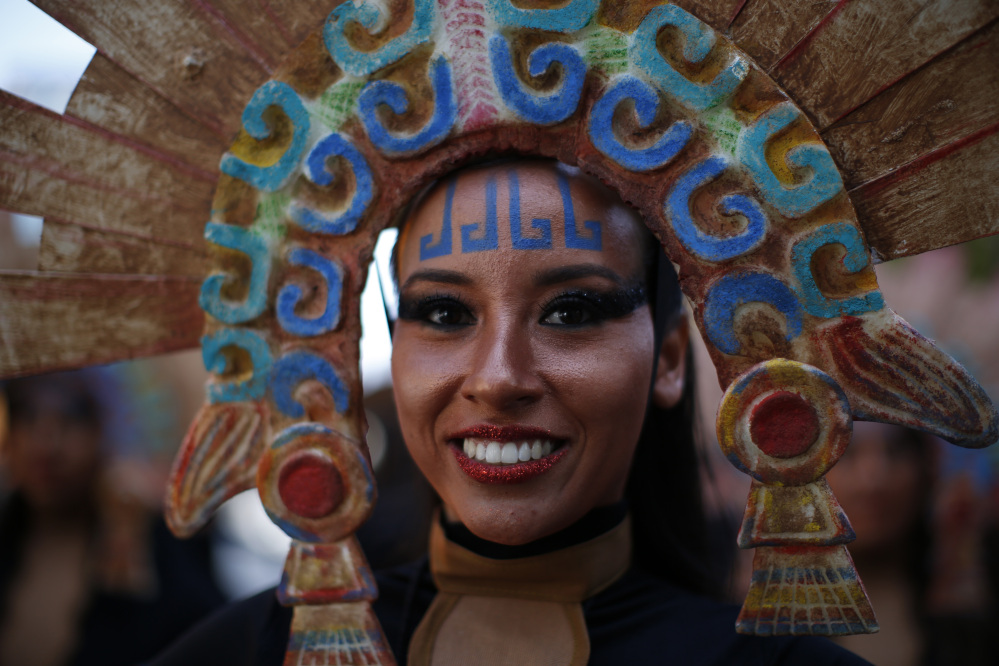 A woman in costume smiles as she waits for the start of a Day of the Dead parade to begin along Mexico City's main Reforma Avenue, Saturday, Oct. 29, 2016. Mexico's Day of the Dead celebrations, which traditionally consisted of quiet family gatherings at the graves of their departed loved ones are fast changing under the influence of Hollywood movies, zombie shows, Halloween and even politics. Mexico's capital was holding its first Day of the Dead parade an idea actually born out of the imagination of a scriptwriter for last year's James Bond movie "Spectre." In the film, whose opening scenes were shot in Mexico City, Bond chases a villain through crowds of revelers in what resembled a parade of people in skeleton outfits and floats. (AP Photo/Dario Lopez-Mills)