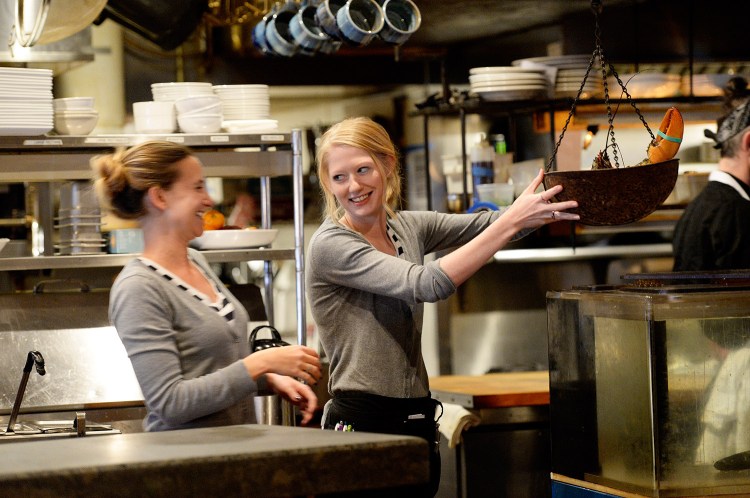 Servers Martina LaChance, left, and Desiree Cofran laugh as LaChance weights a lobster at Boone's Fish House & Oyster Room in Portland on Wednesday. Cofran said a no-tipping policy might work for smaller restaurants, but not high-volume places like Boone’s. She said she can make about $30 an hour on average during a shift. 