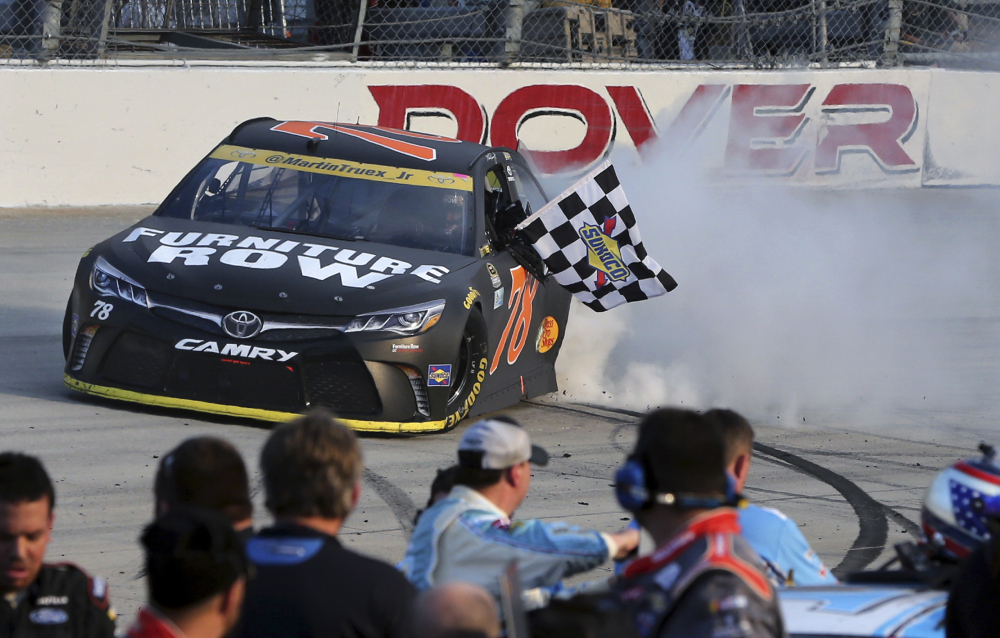 Martin Truex Jr. holds the checkered flag as he does a burnout after winning a NASCAR Sprint Cup Series race Sunday at Dover International Speedway in Dover, Delaware. Kyle Busch (18) was second.