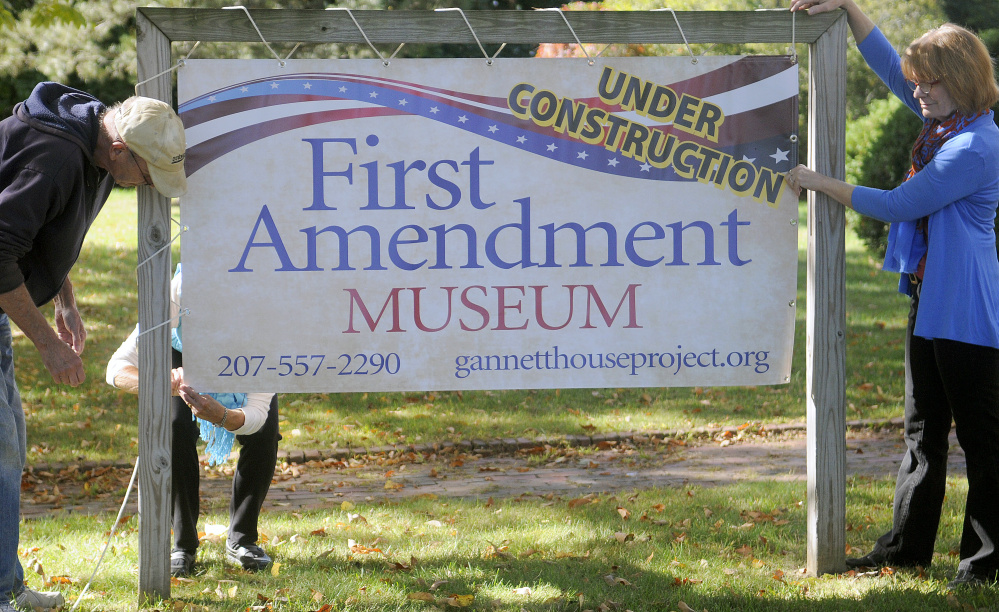 Genie Gannett, right, hangs a sign Monday for the First Amendment Museum in front of the Gannett House in Augusta with Denis Thoet, left, and Susan Gross.