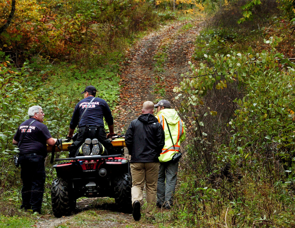 Skowhegan firefighters transport a gurney to the scene where the body was found Sunday off a remote trail in Skowhegan. Authorities on Monday identified the man as Gary Lisherness, 56, of Madison.