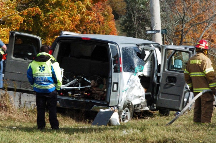 State police and firefighters investigate the scene beside a van filled with nine passengers and operated by the College of the Atlantic after it collided with another vehicle at the intersection of Route 220 and the Crosby Brook Road in Thorndike on Sunday.