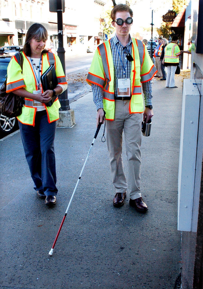 Stacie Beyer watches as Ben Lake navigates sidewalks on Main street in Waterville during a GrowSmart Maine annual conference on Wednesday. Lake was using a walking cane and wore glasses that inhibited vision to illustrate challenges to visually impaired people.
