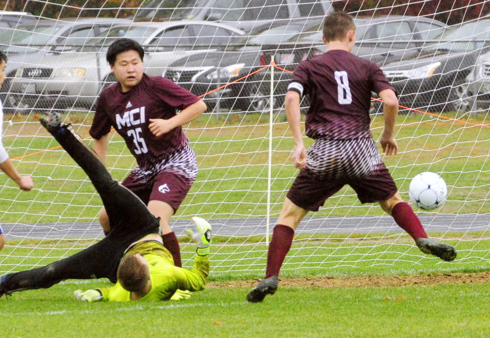 Erskine keeper David McGraw flips after making a save but MCI's Devon Varney (8) scores the game-winning goal in the second overtime of a Class B North preliminary game Saturday in South China. MCI's JunSu Jang (35) looks on.