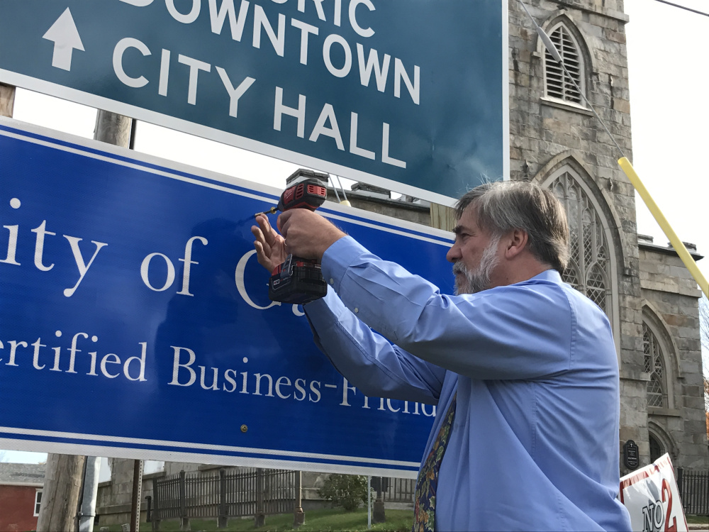 Gardiner Mayor Thom Harnett sets a screw in the city's Certified Business-Friendly sign Thursday on a post near the corner of Brunswick and Dresden avenues.