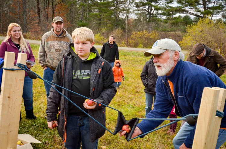 Lukkas Whitman, of Clinton, learns from Mark "Mac" McAfee, of Belgrade, how to use the apple slingshot Saturday at the Fall Festival on Saturday at the Quarry Road Trails recreation area in Waterville.