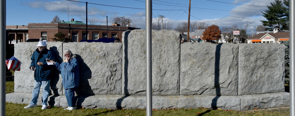 A couple finds relief from the wind Friday behind the veterans' memorial wall during a re-dedication of Veterans Memorial Park in Skowhegan.