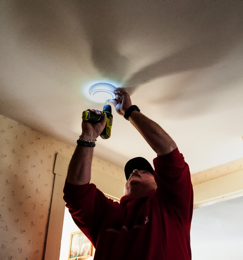 The light from his drill illuminates Randolph Fire Dept. Capt. Jim Kimball as he installs a smoke alarm on Saturday in a Randolph home.