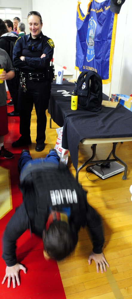 Augusta police school resource officer Carly Wiggin watches as a student tries to see how many push-ups he can do while wearing a tactical vest during a college and career fair Thursday at Cony High School. Students were trying to do the same thing at the U.S. Marine Corps booth.