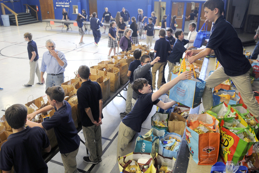 St. Michael eighth-graders Chris Bourdon, right, and Dom Brunelle prepare bags of groceries Monday for the Thanksgiving holiday at the private Catholic school in Augusta. Several people collected the donated meals assembled by the students.