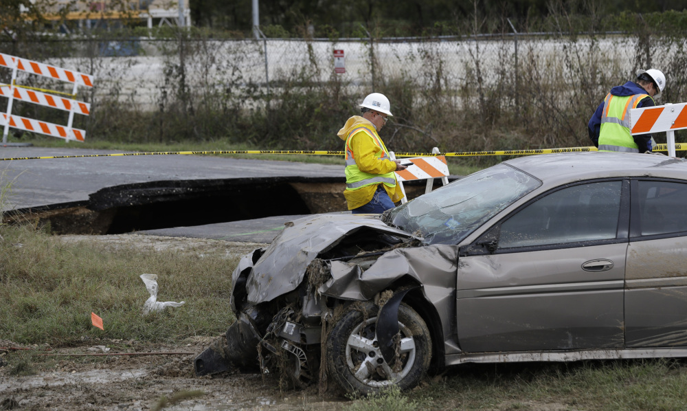 A worker walks past a sinkhole and a car that was pulled from it on Monday in San Antonio. Officials say an off-duty sheriff's deputy has died and two other people hurt when the vehicles plunged into the water-filled sinkhole.