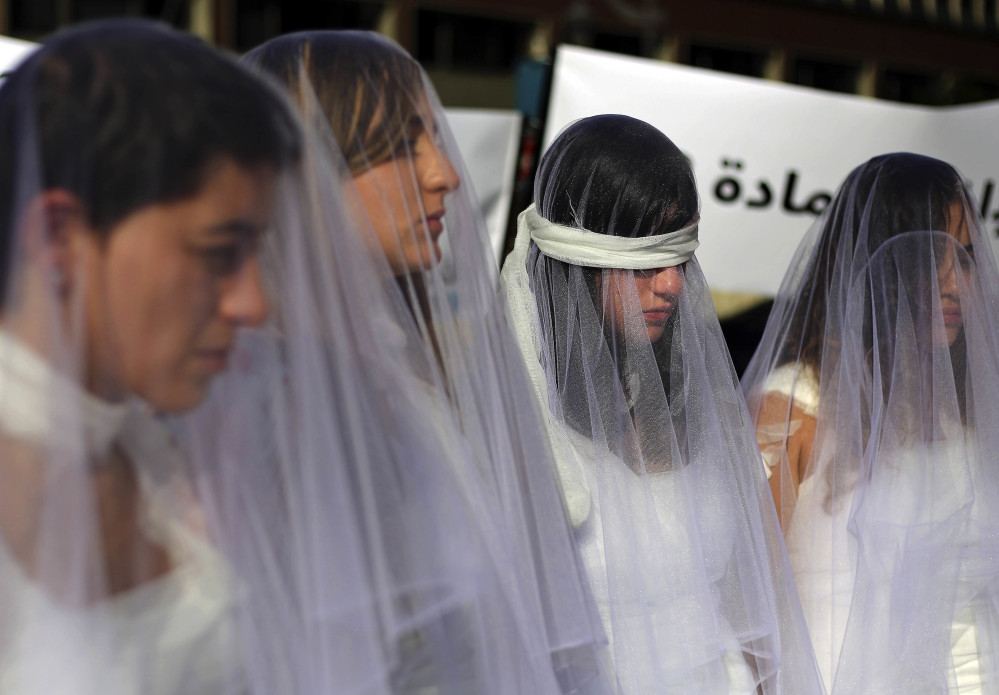 Lebanese women in wedding gowns stained with fake blood, some wearing bandages, stand in front of a government building in Beirut, Lebanon, on Tuesday. They called for repeal of a law allowing a rapist to go free if he marries his victim.