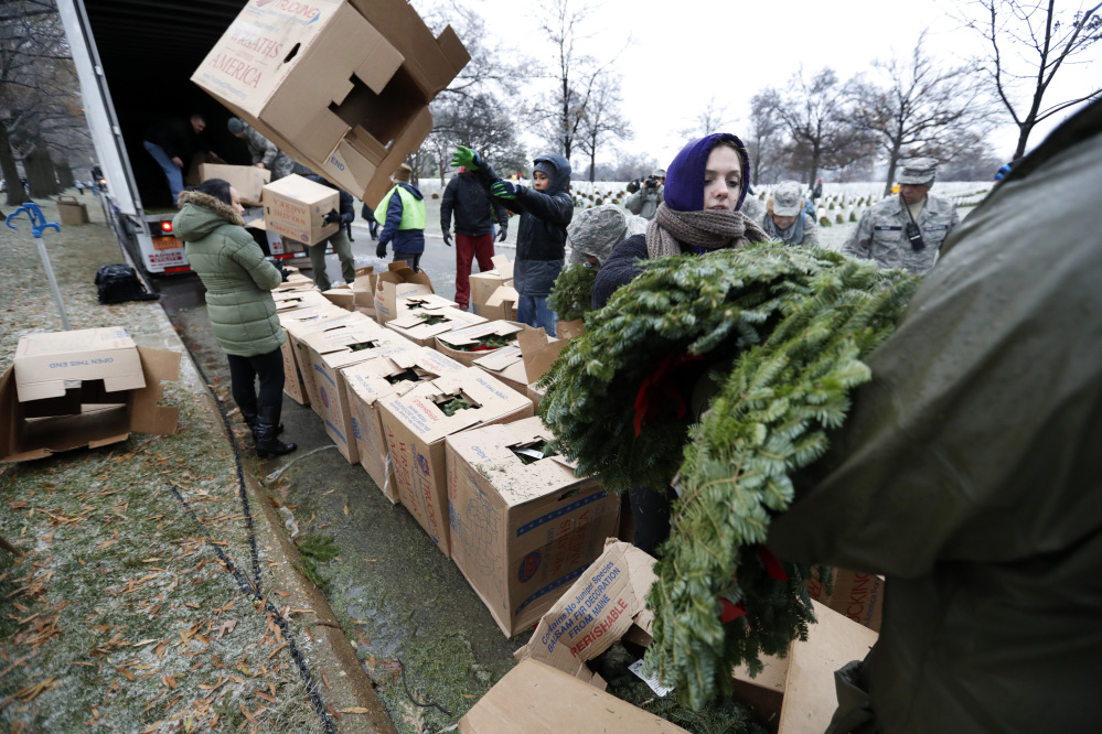 Volunteer Alyssa Kane of Alexandria, Va., passes out wreaths to be placed at graves as part of Wreaths Across America at Arlington National Cemetery, Saturday, Dec. 17, 2016 in Arlington, Va. Organizers estimate more than 245,000 wreaths were placed at graves throughout the cemetery. (AP Photo/Alex Brandon)