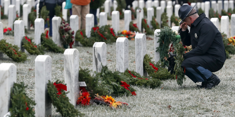 Maine State Police Detective Chad Lindsey pauses at a friend's grave in Section 60 as he carries a wreath to be placed at another grave, during Wreaths Across America at Arlington National Cemetery, Saturday, Dec. 17, 2016 in Arlington, Va. Organizers estimate more than 245,000 wreaths were placed at graves throughout the cemetery. (AP Photo/Alex Brandon)